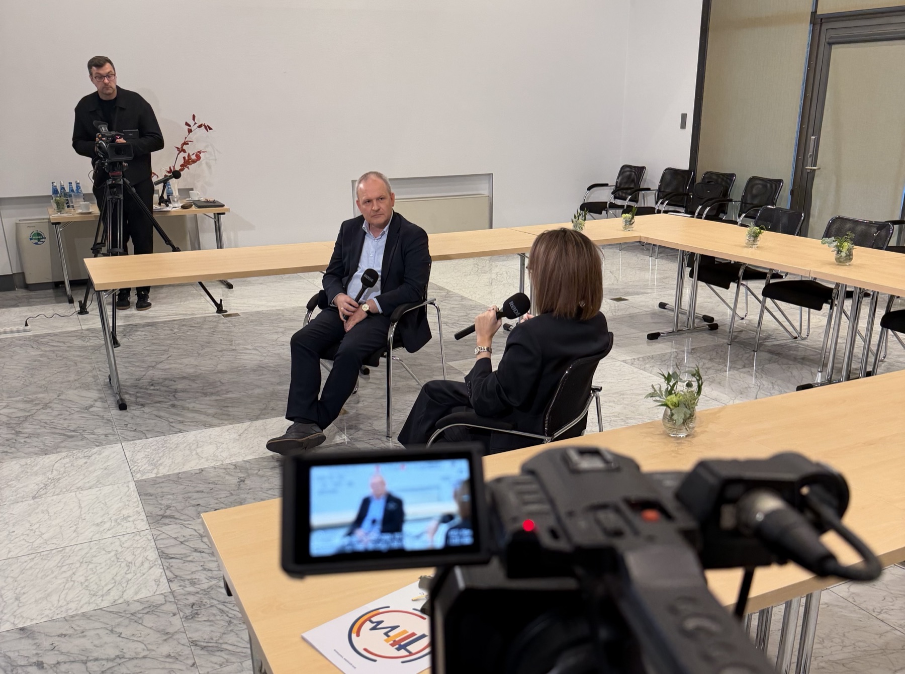 Nagranie rozmowy na dwie kamery: dwie osoby w fotelach z mikrofonami, operator przy kamerze na statywie