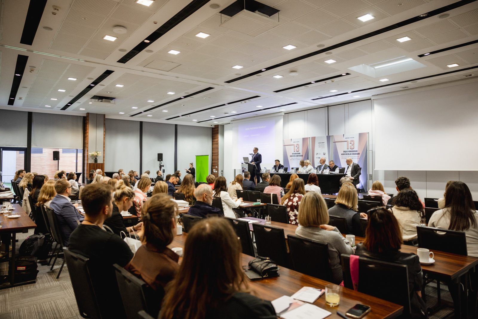 Sala konferencyjna widziana z tyłu, na scenie panel prelegentów