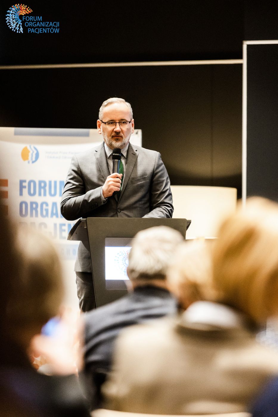 Wystąpienie przy mównicy, na pierwszym planie publiczność