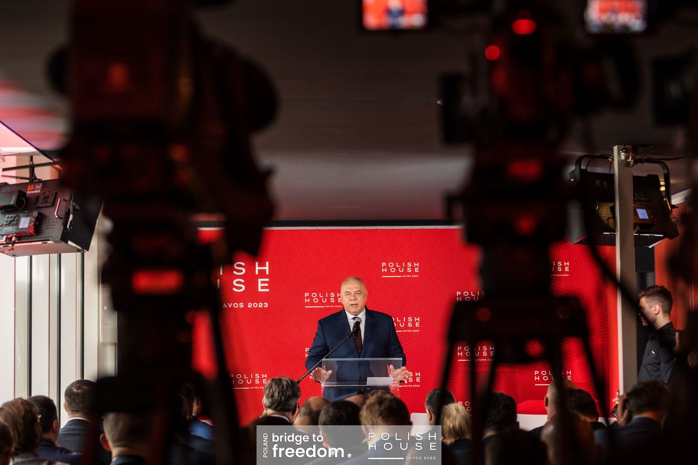 Wystąpienie przy mównicy, na pierwszym planie kamery