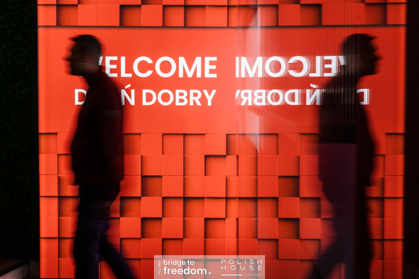 Goście przechodzą przed ścianą z napisem Welcome, dzień dobry
