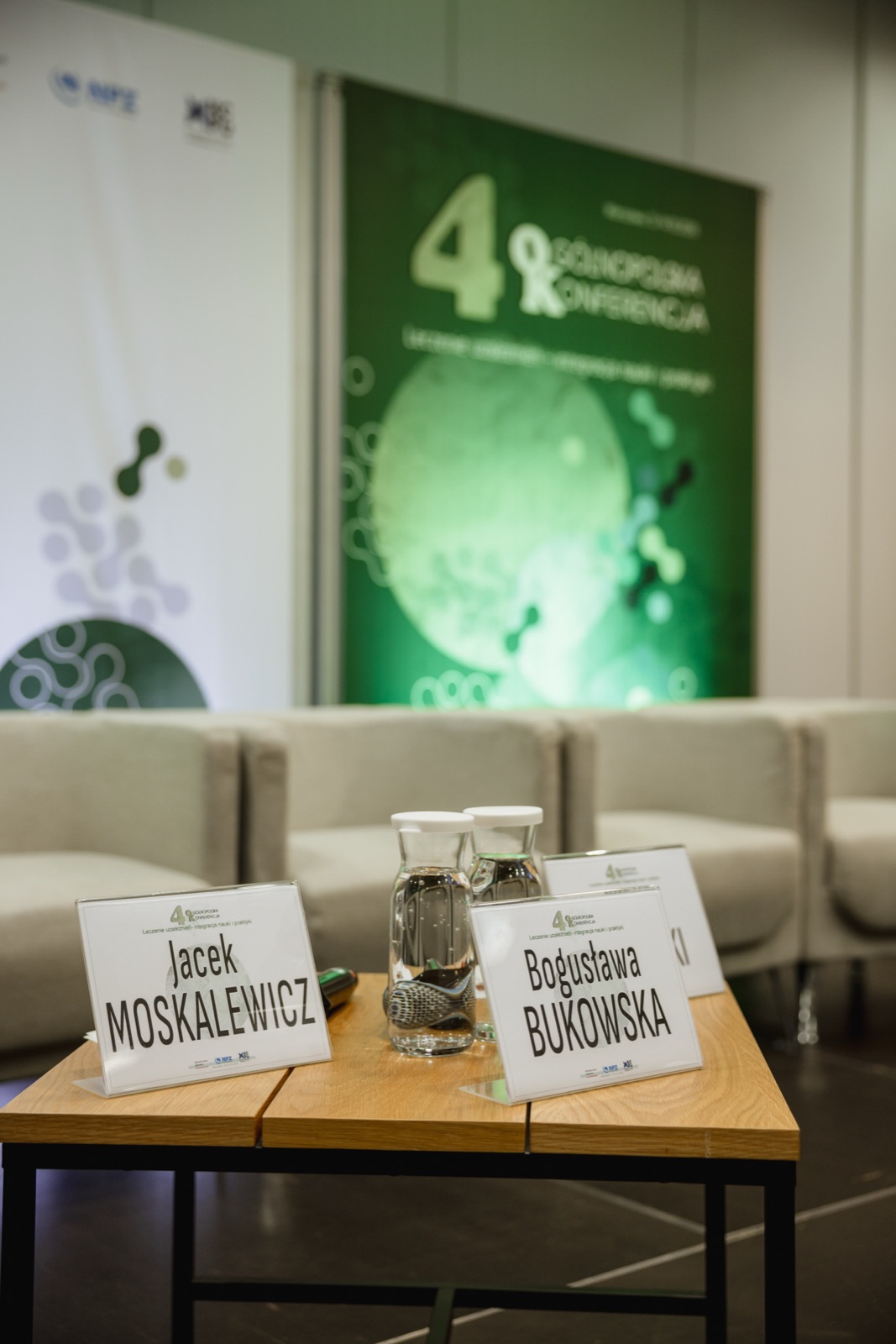 Stolik prelegentów z identyfikatorami przed zieloną ścianką konferencji