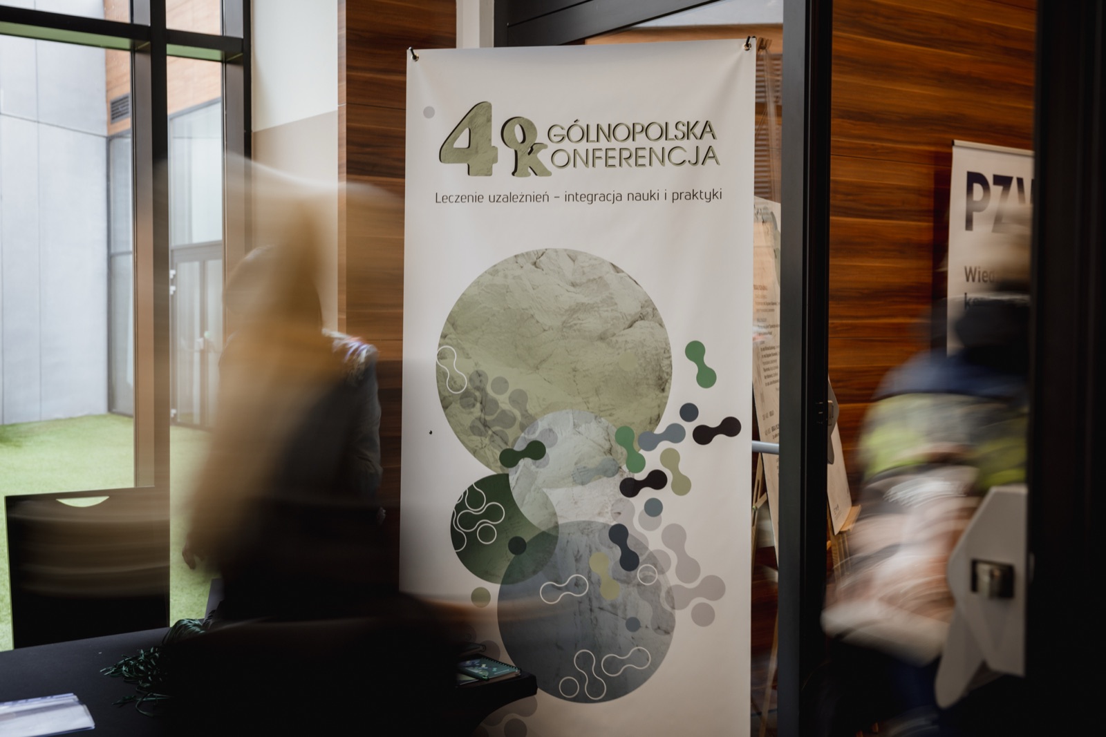 Roll-up konferencji w holu, w tle rozmyte sylwetki przechodzących osób