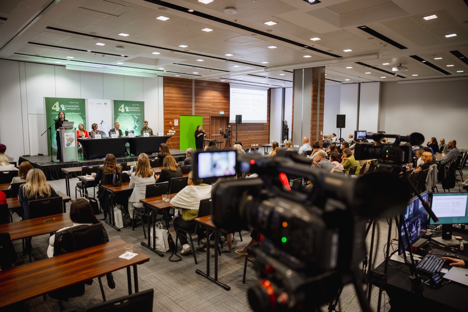 Kamera i stanowisko realizacji w sali konferencyjnej, na scenie prelegentka i tłumaczka języka migowego